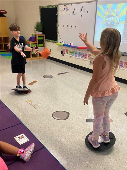 Two elementary children playing catch on balancing discs.